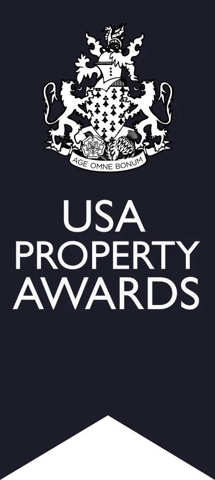 Alt text: "Logo of the USA Property Awards featuring a detailed crest with a heraldic design and the slogan 'Age Omne Bonum,' set against a dark blue background, emphasizing prestige in the real estate industry."