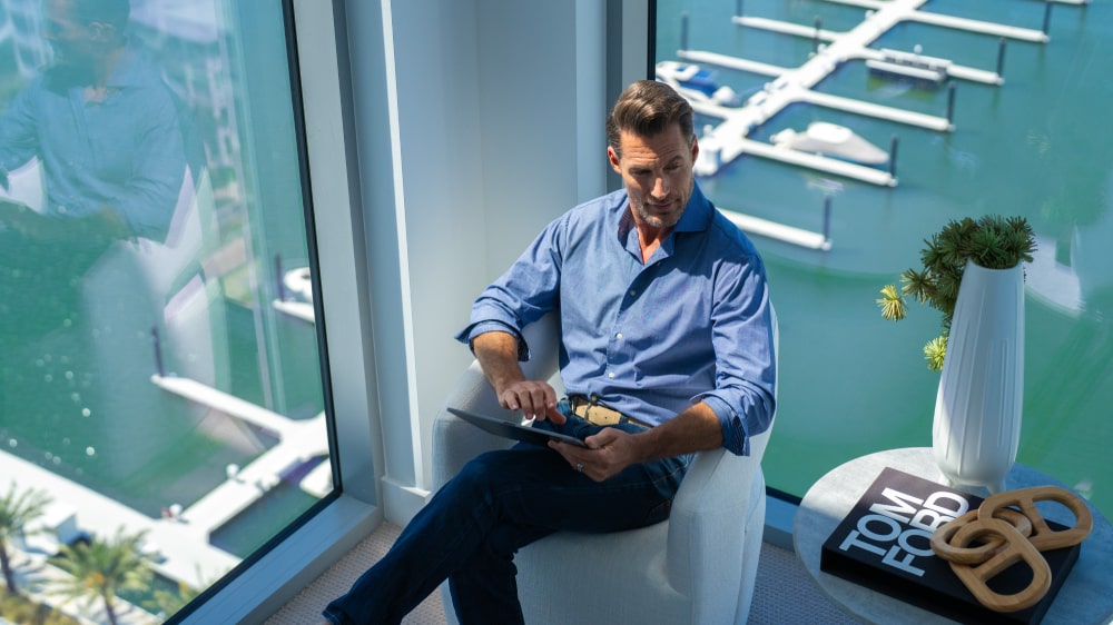 Man sitting by the window overlooking the Marina Pointe marina from a luxury condo