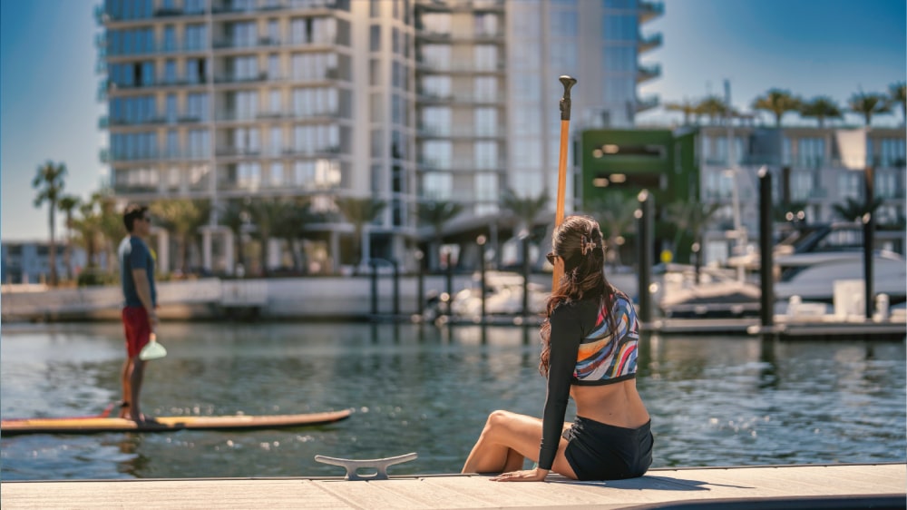 Woman sitting on the dock with paddleboarders in front of Marina Pointe residences
