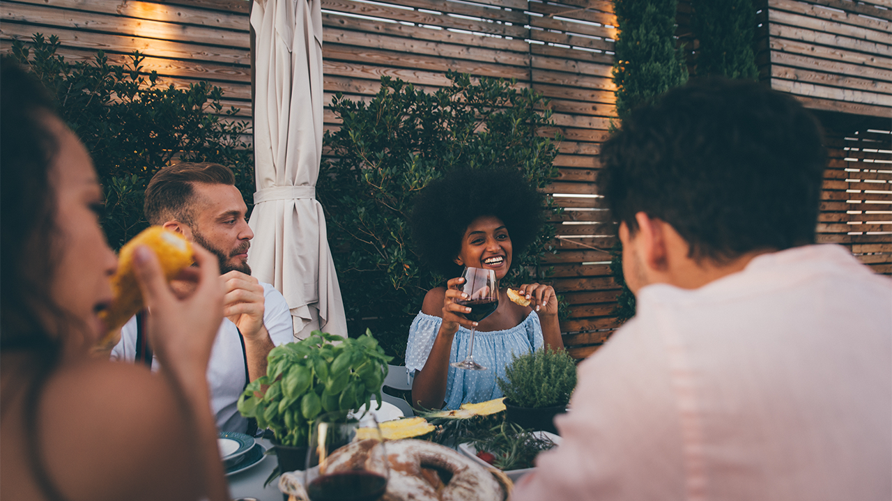 Group of friends enjoying wine and food outdoors at a cozy dining table.