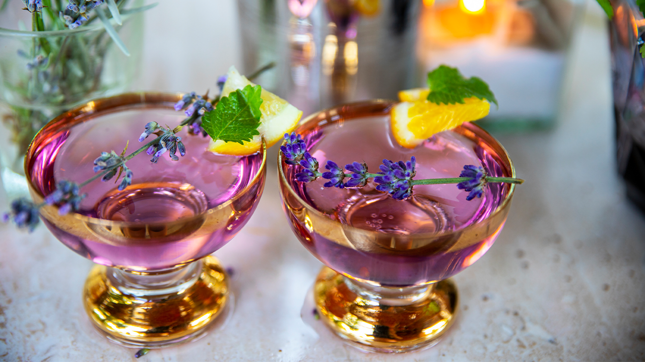 Purple lavender cocktails garnished with citrus slices and fresh herbs.
