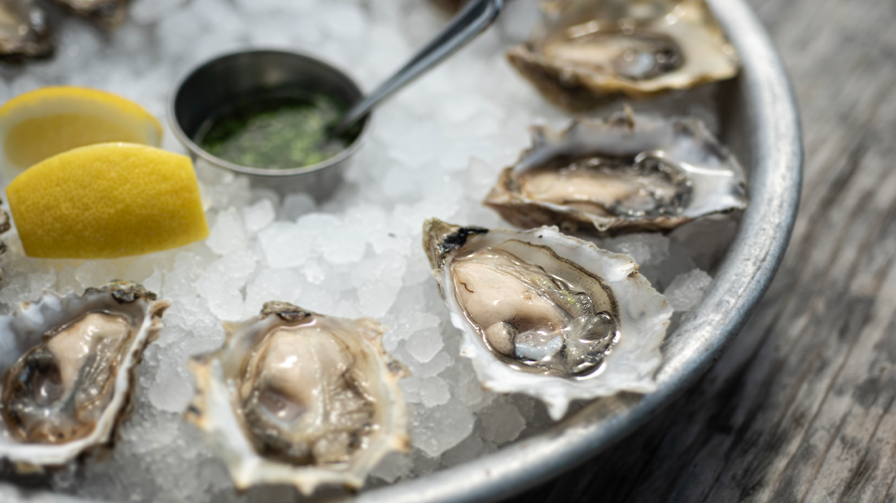 Plate of fresh oysters on ice with lemon wedges and sauce.