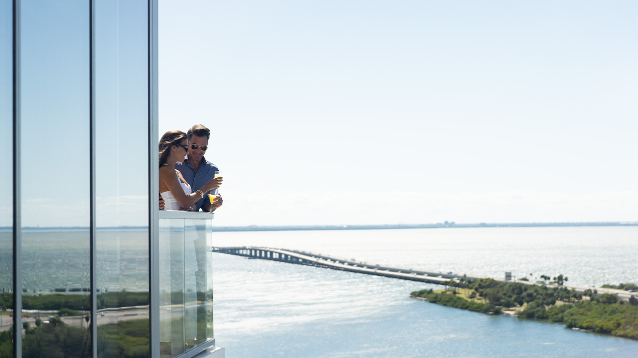 Couple enjoying drinks on a high-rise balcony overlooking Tampa Bay and the causeway.