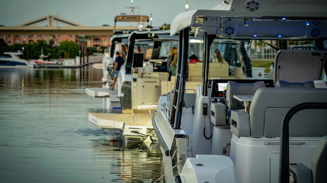 Row of docked boats lined up on calm water near a marina walkway.