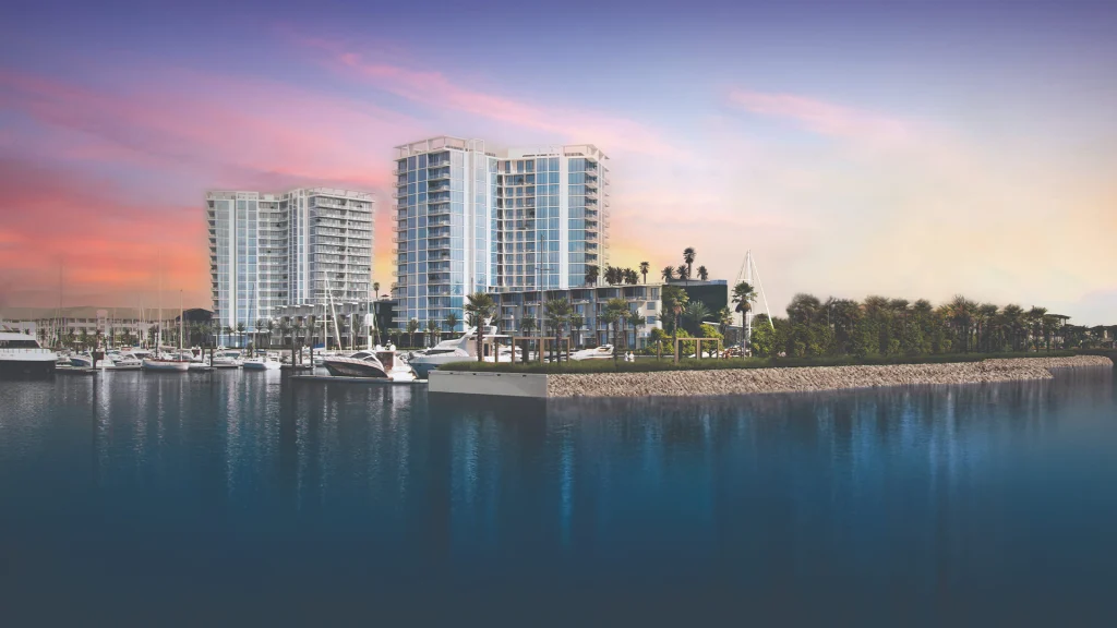 Waterfront condo towers beside a marina at sunset with boats and palm trees.